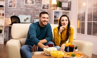 A couple watching TV with popcorn from behind the sofa